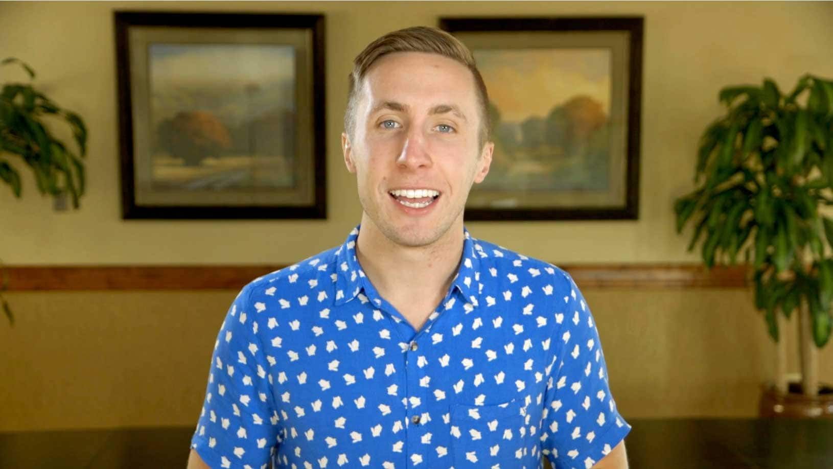 A man in a blue shirt is standing in front of a table and smiling.