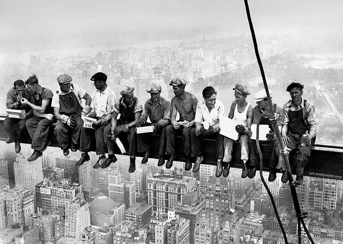 A group of men are sitting on a ledge overlooking a city.