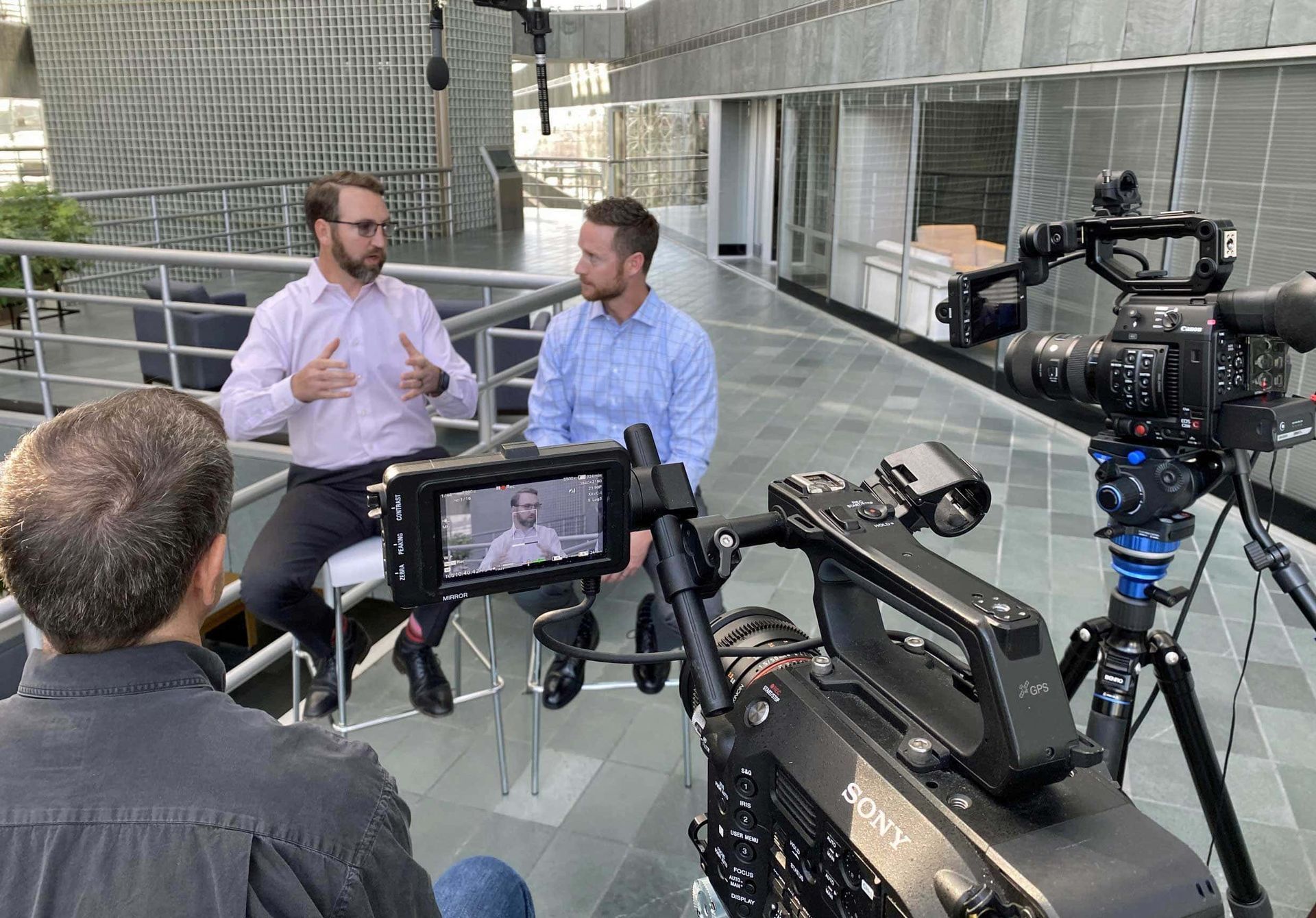 Two men are sitting in front of a camera talking to each other.