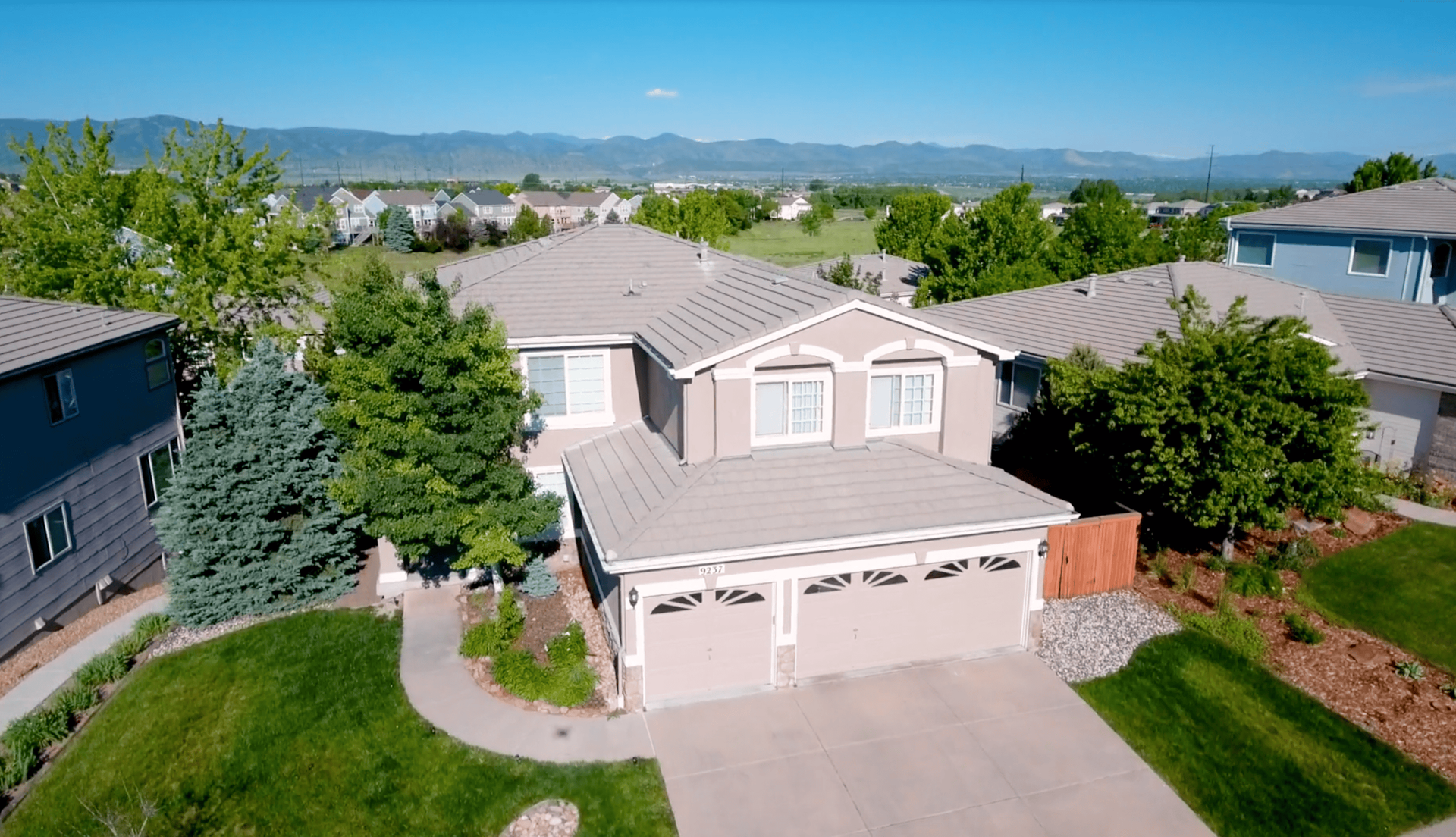 An aerial view of a house in a residential area with mountains in the background.