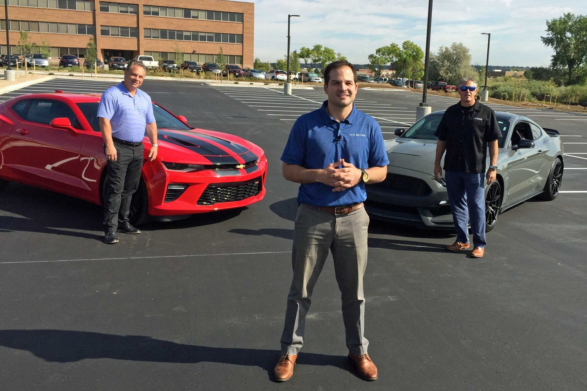 Three men are standing in a parking lot in front of cars