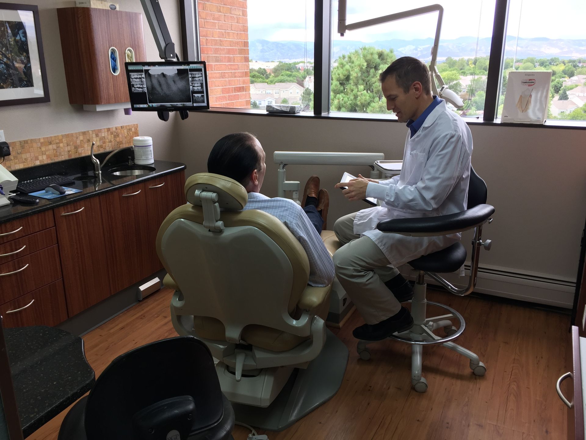 A man is sitting in a dental chair talking to a dentist.