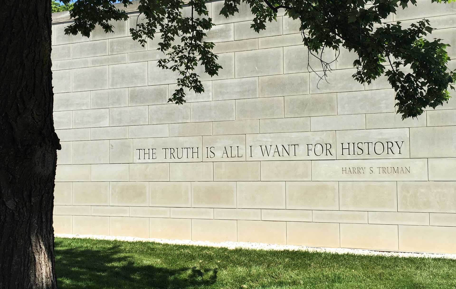A brick wall with a tree in the foreground and a quote on it