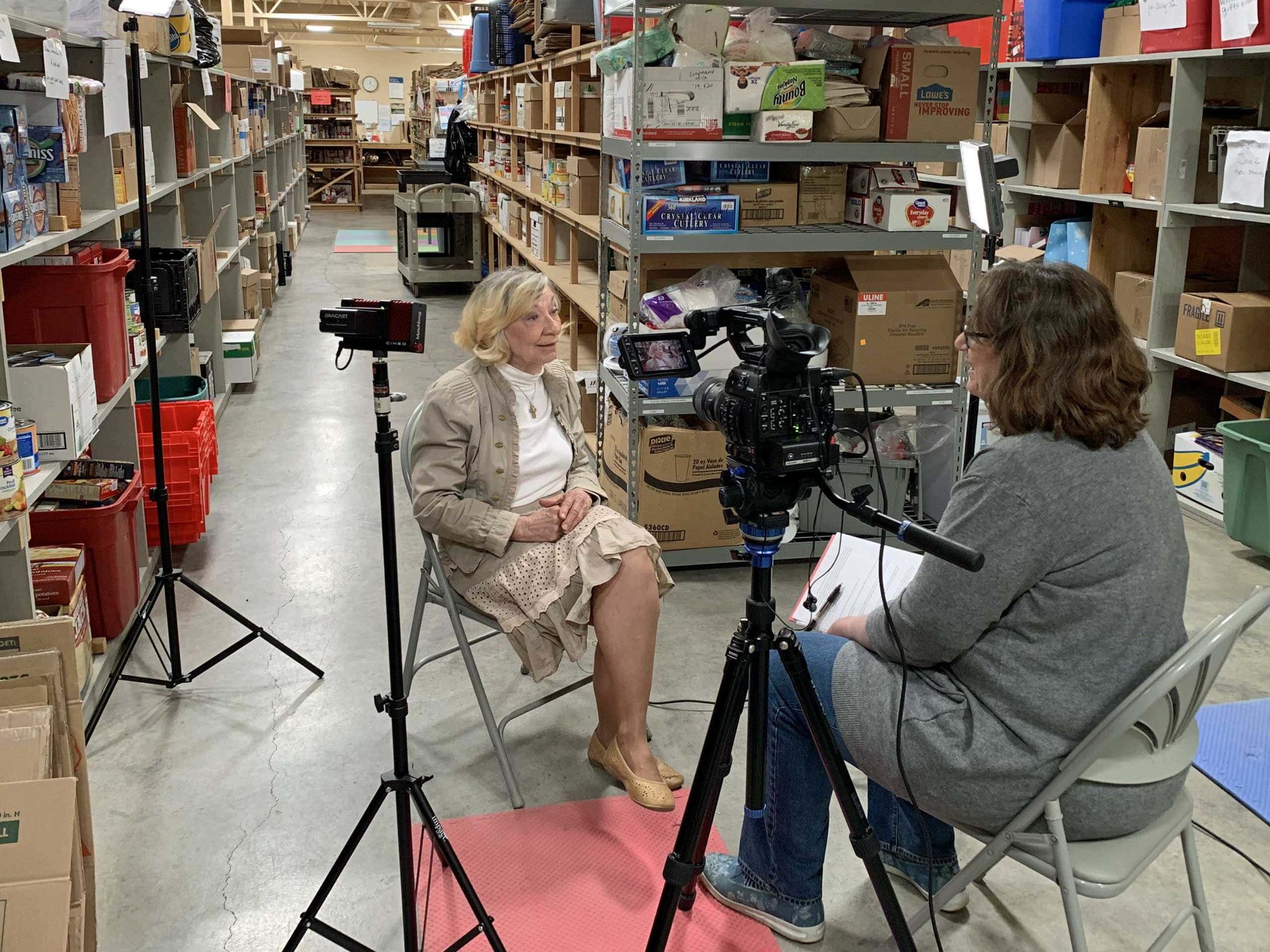 A woman is sitting in front of a camera in a warehouse
