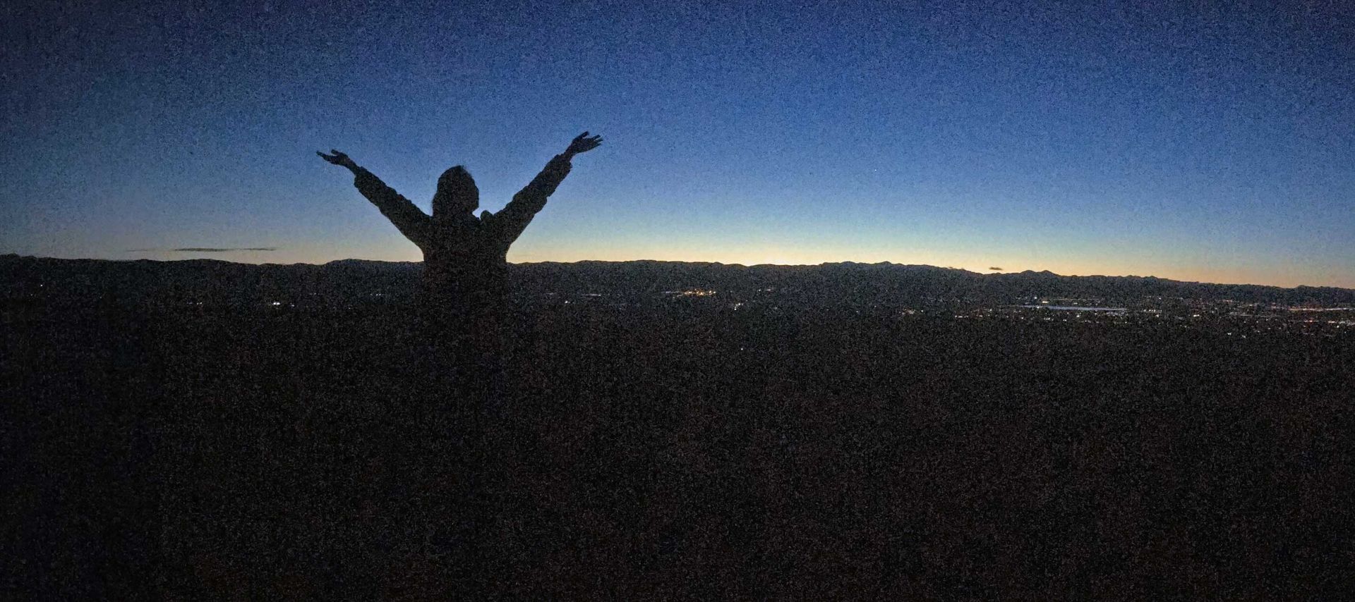 A silhouette of a person standing in a field with their arms outstretched.