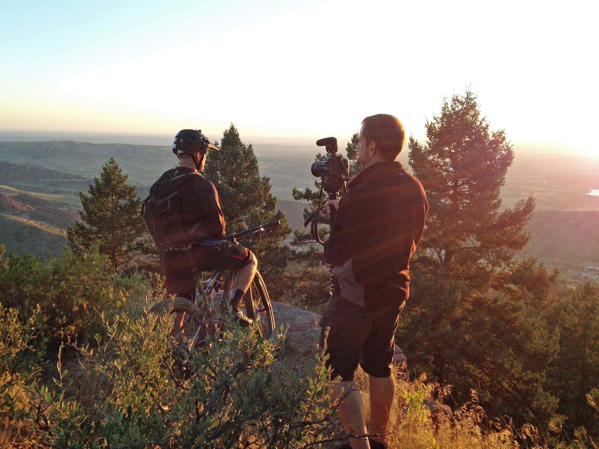 Two men are standing on top of a hill with cameras.