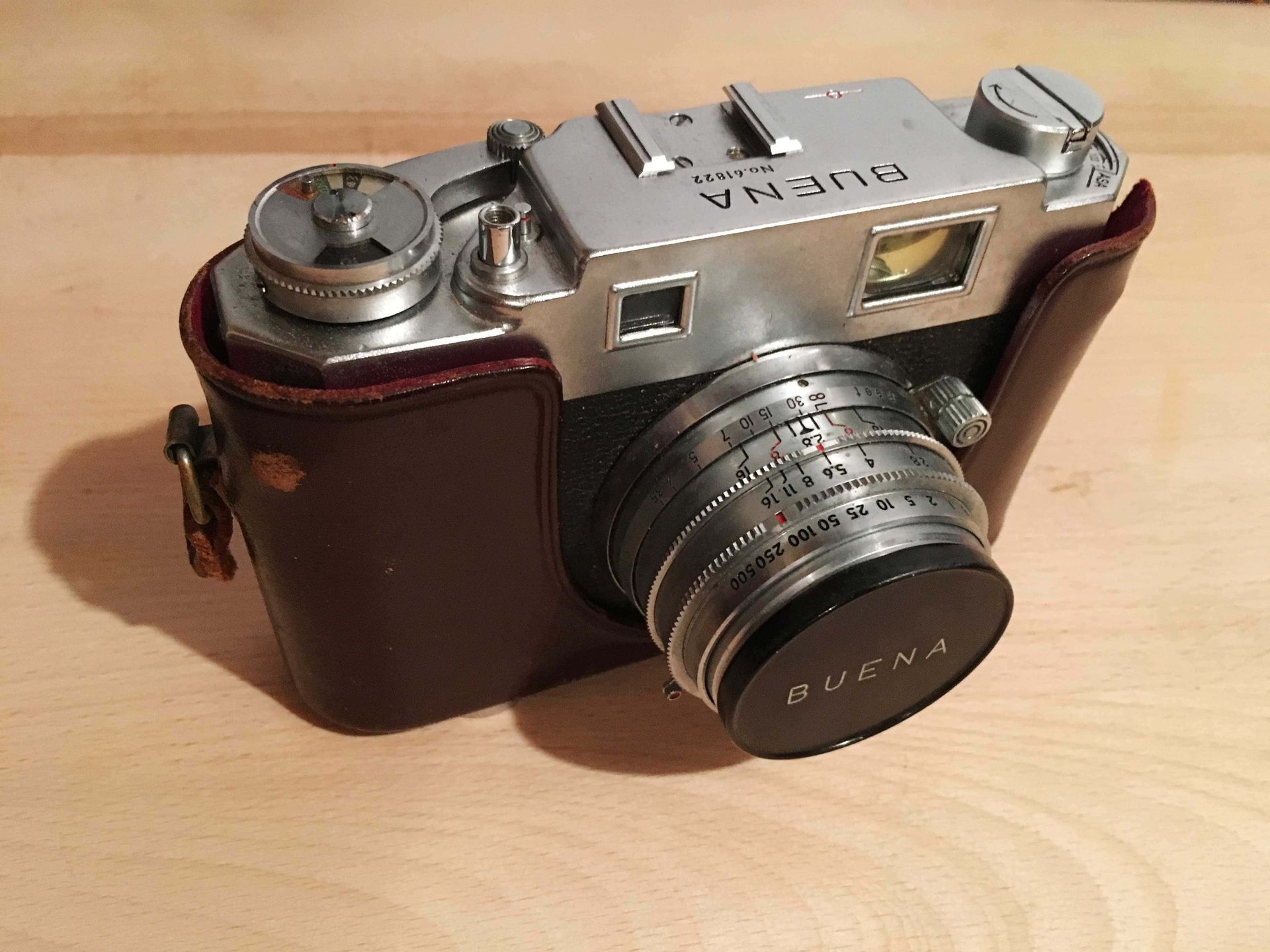 An old camera with a leather case is sitting on a wooden table.