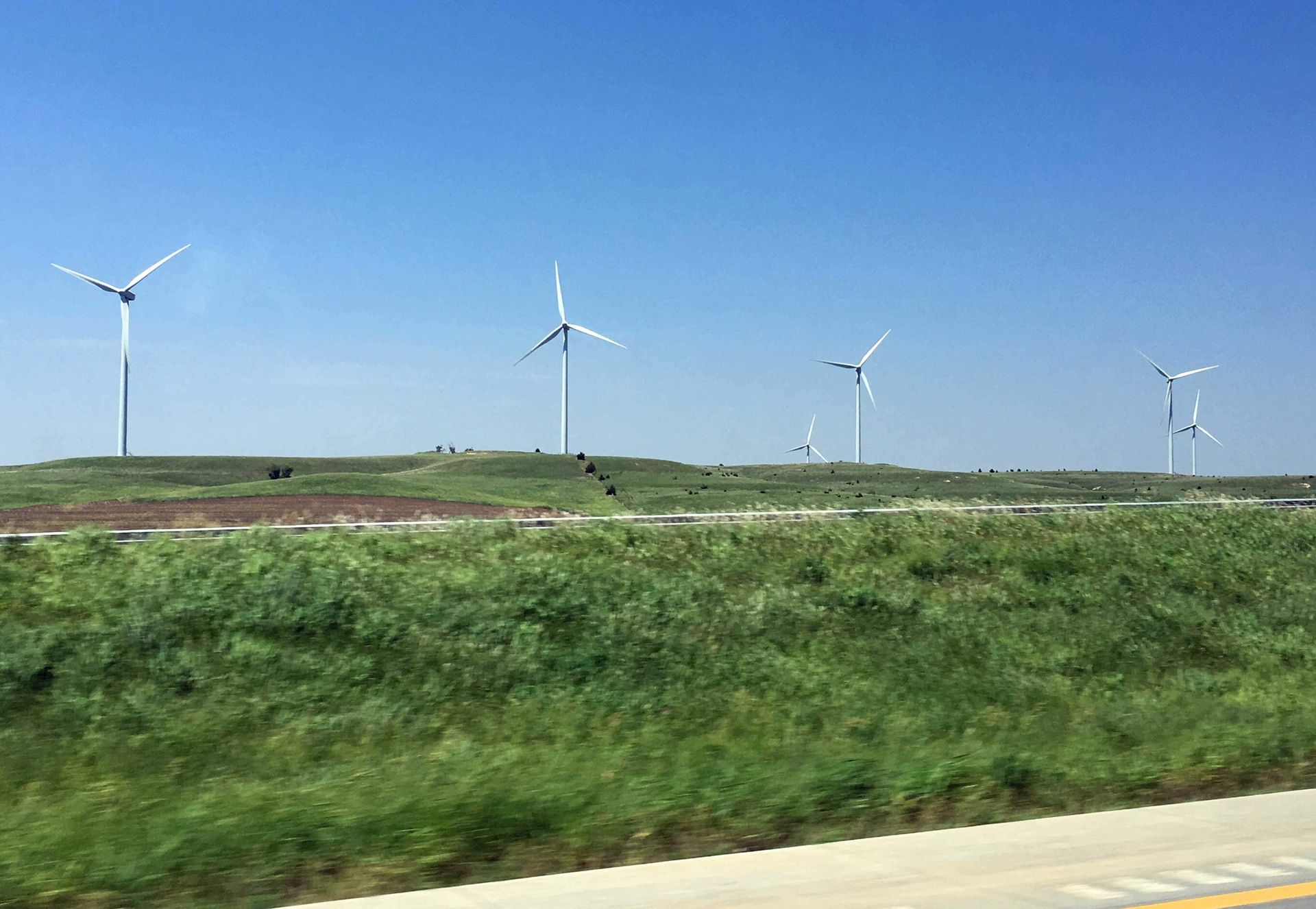 A row of wind turbines are sitting on top of a grassy hill.