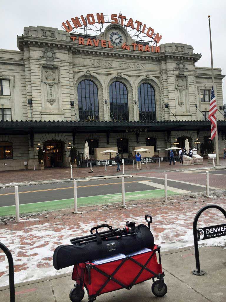A red wagon is parked in front of a large building.