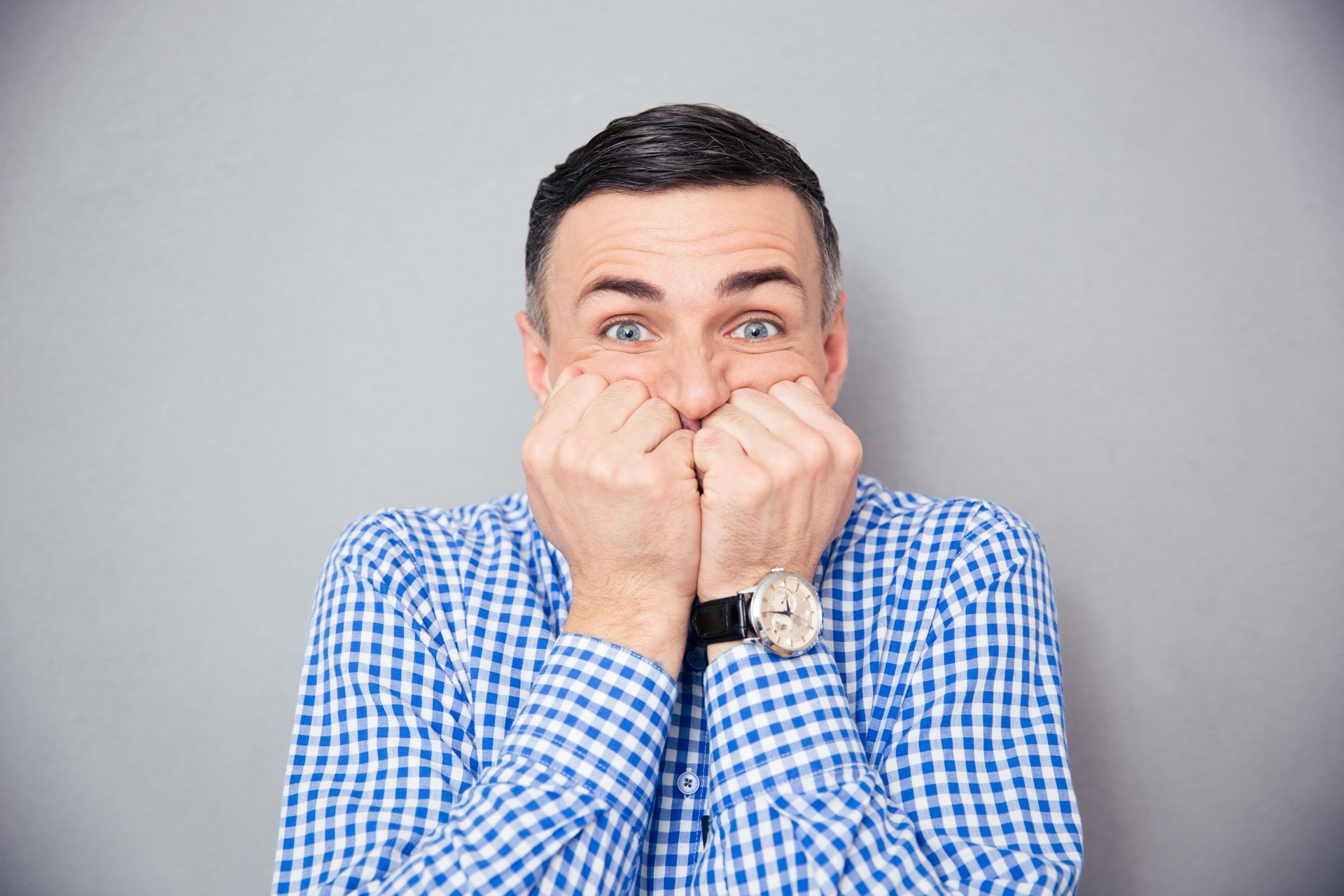 A man in a plaid shirt is covering his mouth with his hands.