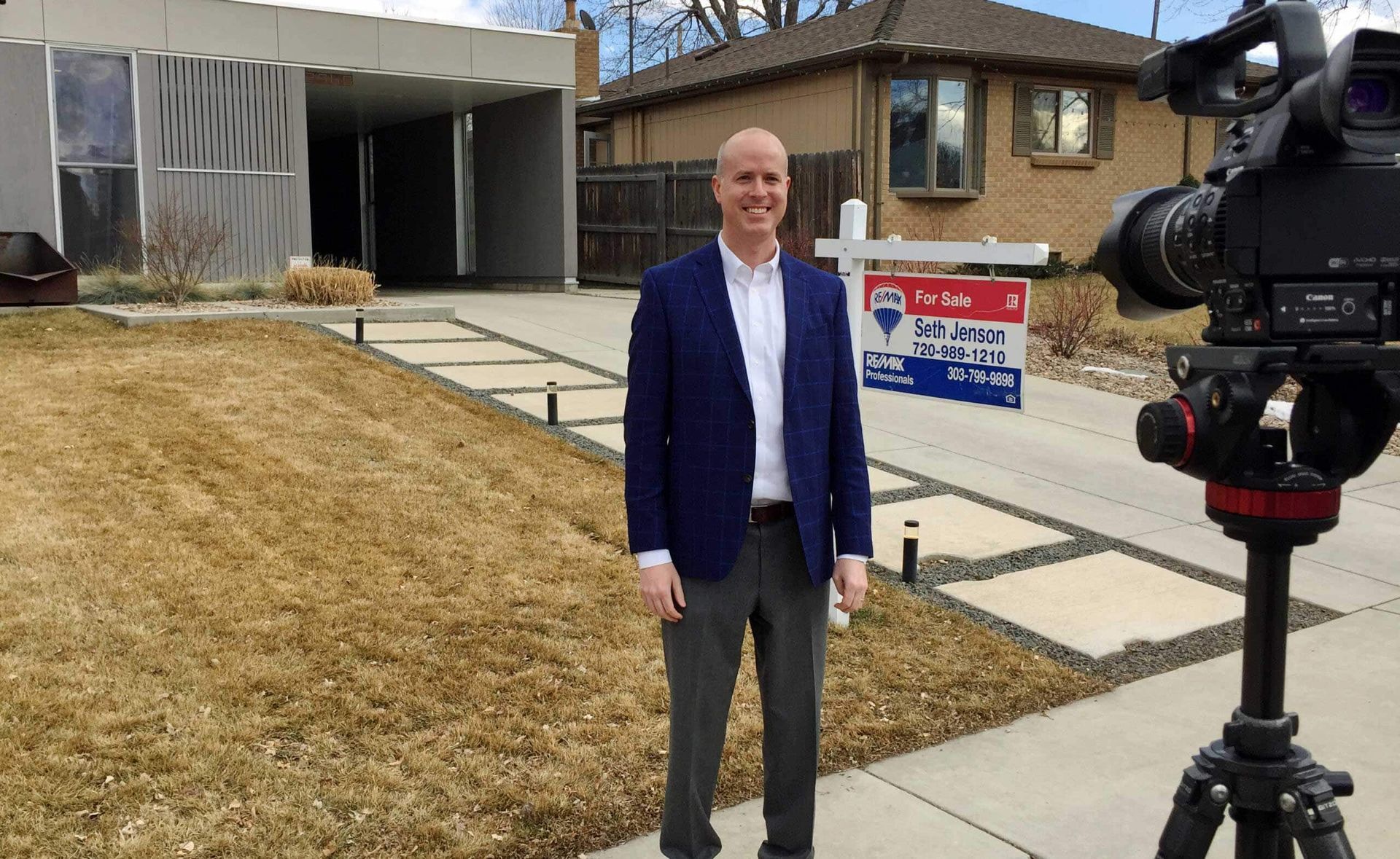 A man in a suit is standing in front of a for sale sign