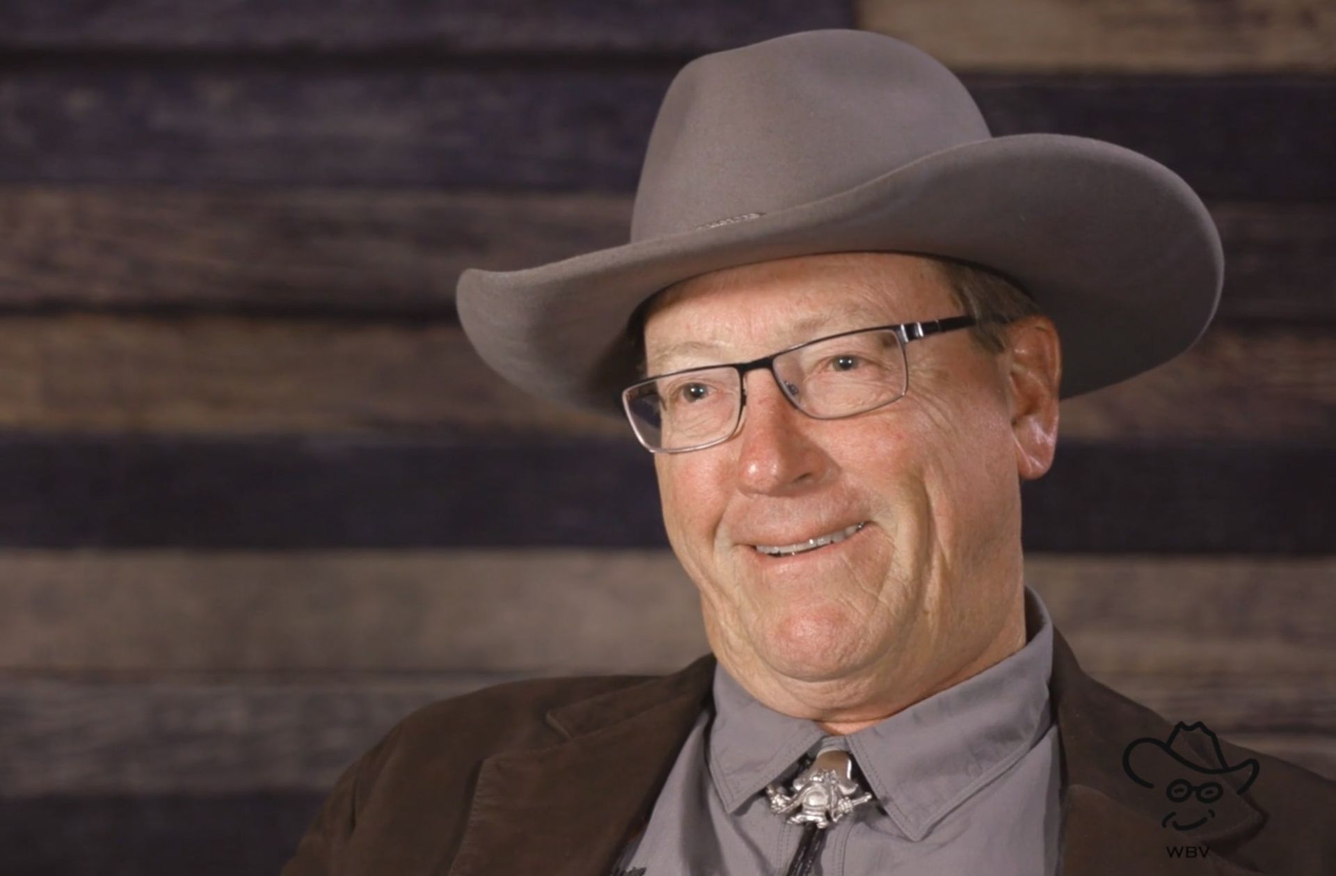 A man wearing a cowboy hat and glasses is smiling.