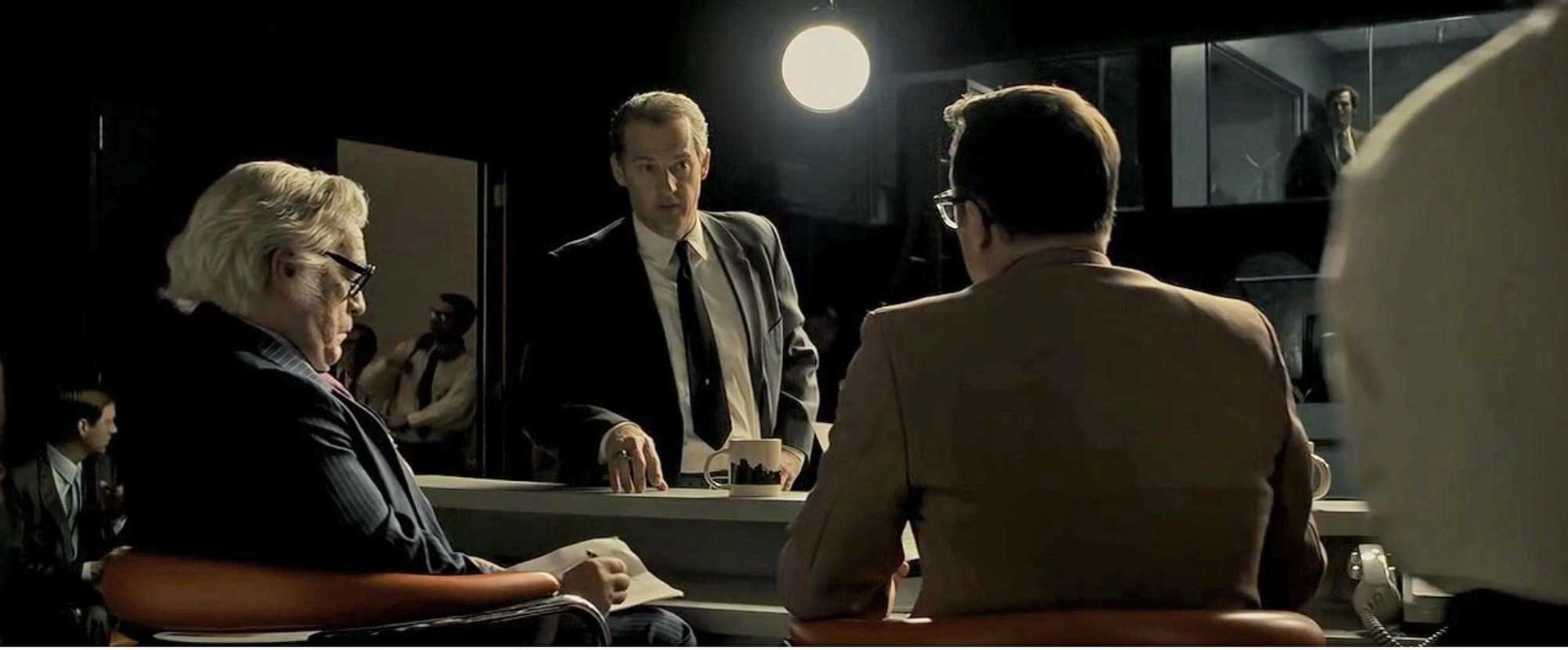 A group of men are sitting in a dark room talking to each other.