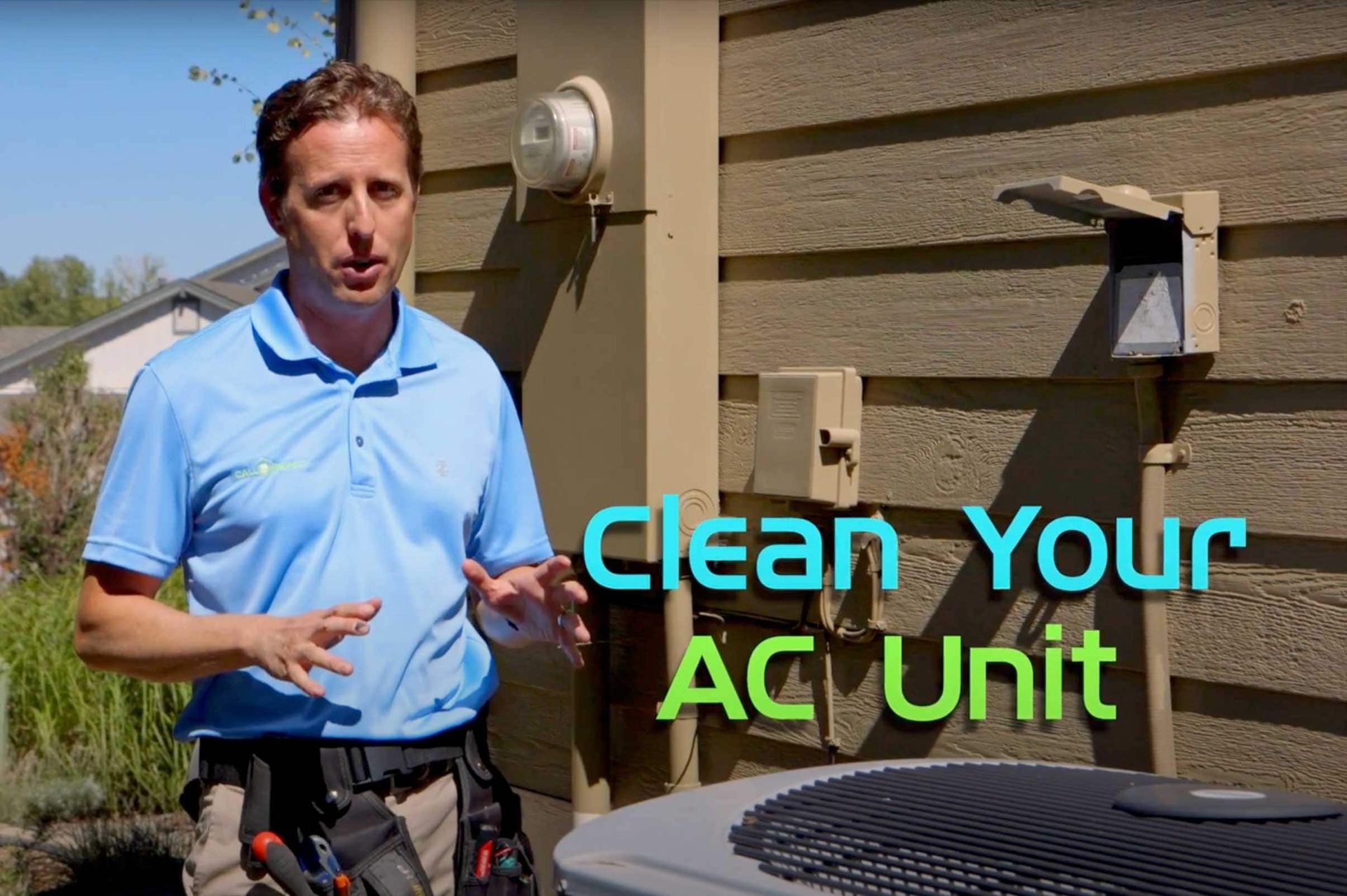 A man in a blue shirt is standing in front of an air conditioner.