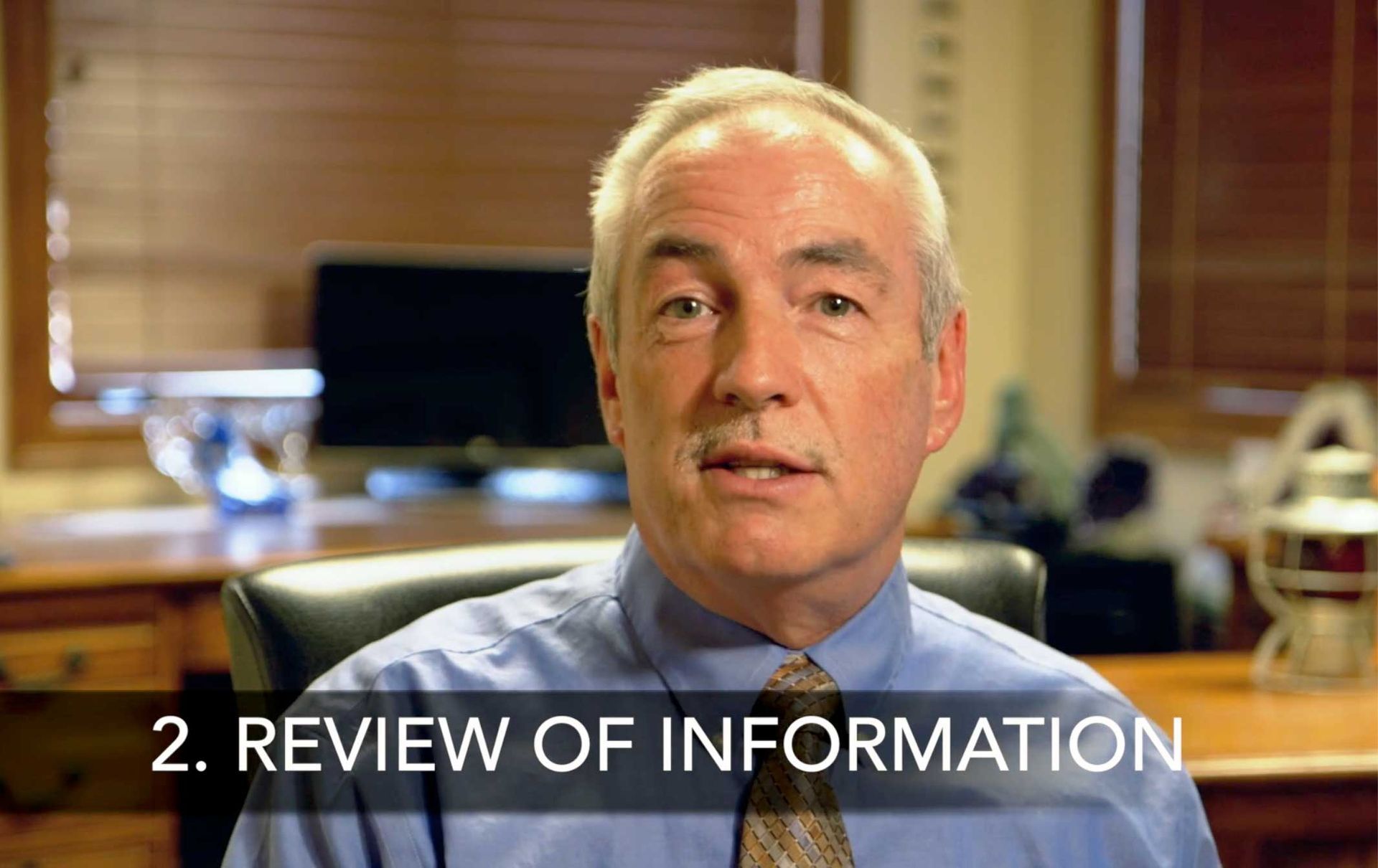 A man in a blue shirt and tie is sitting in a chair with the words review of information below him