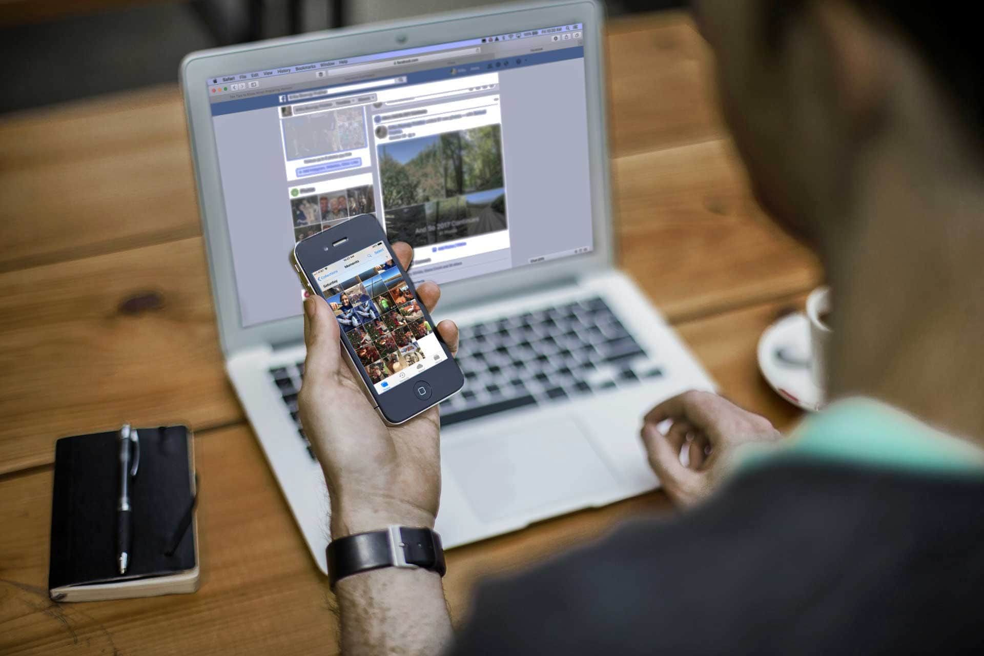A man is holding a cell phone in front of a laptop computer.