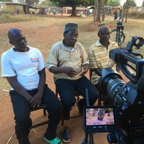 Three men are sitting in front of a camera and one of them is wearing a shirt that says ' united states ' on it
