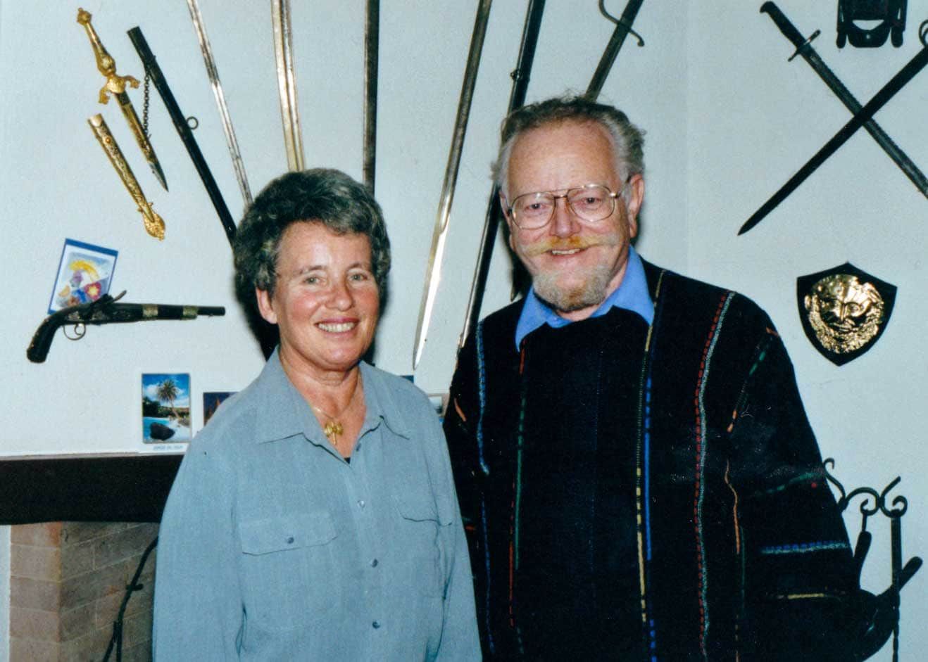 A man and a woman are posing for a picture in front of a wall full of swords and shields