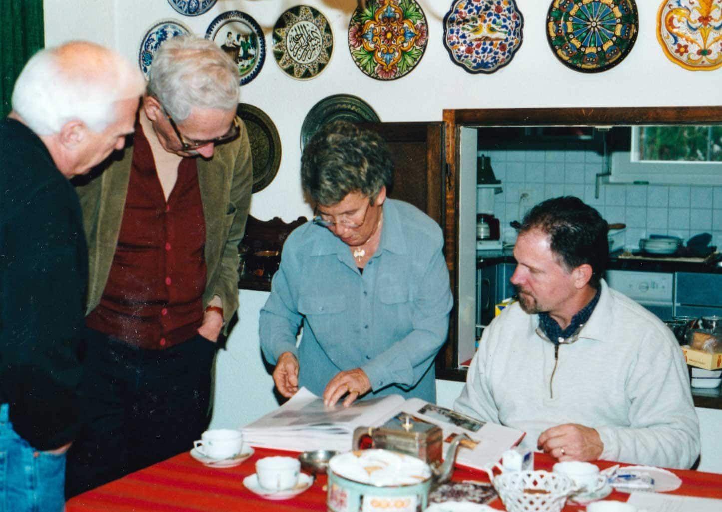 A group of people are gathered around a table with plates on the wall behind them