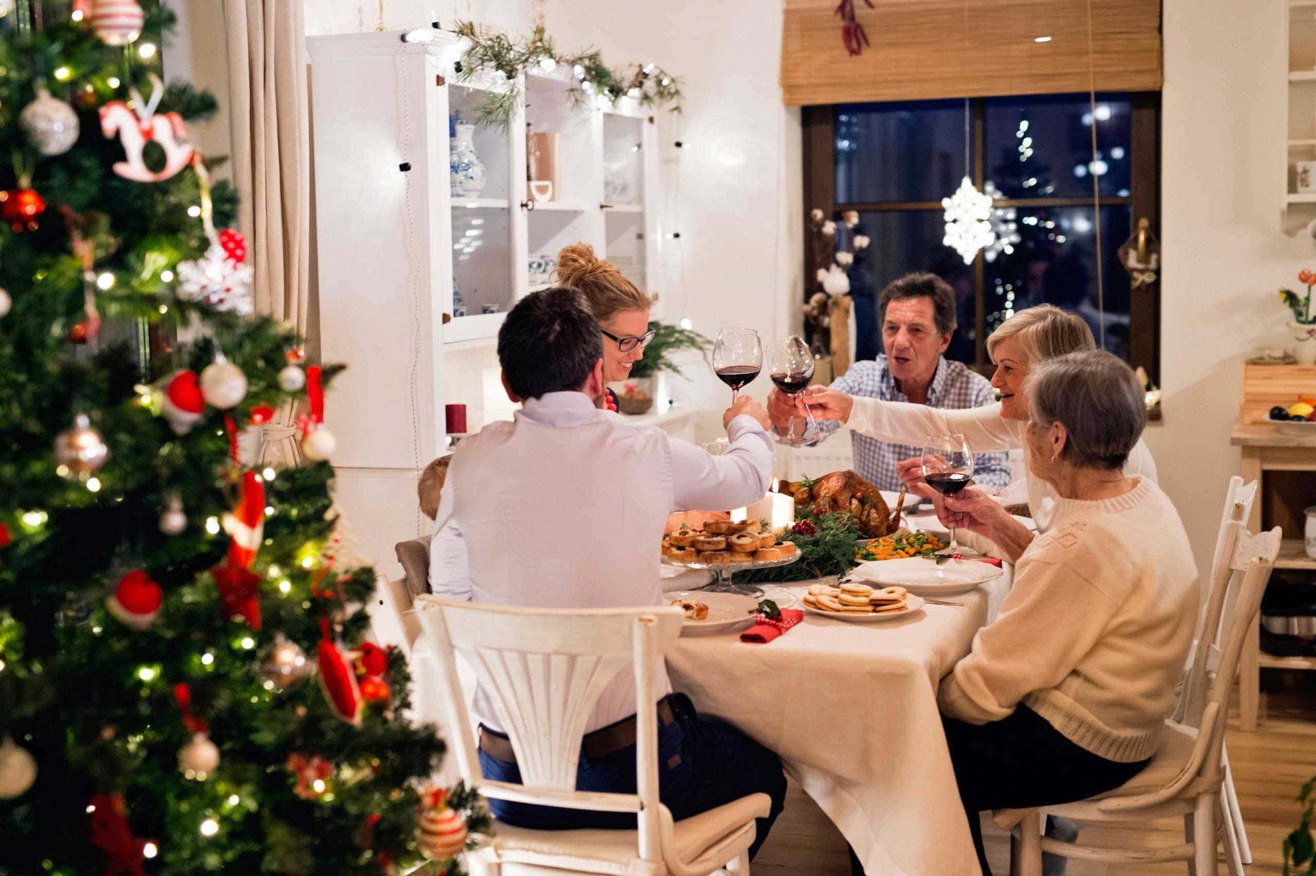 A group of people are sitting at a table with a christmas tree in the background.