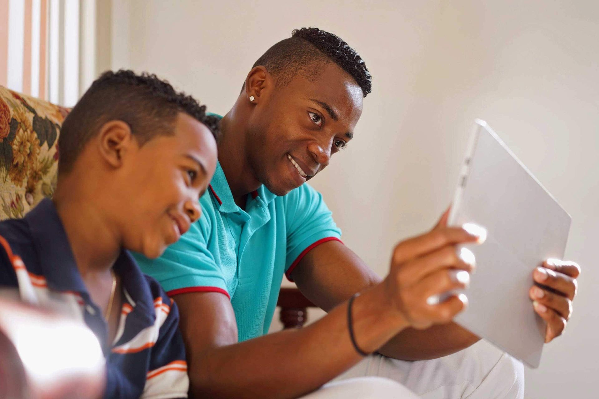 A man and a boy are sitting on a couch looking at a tablet.