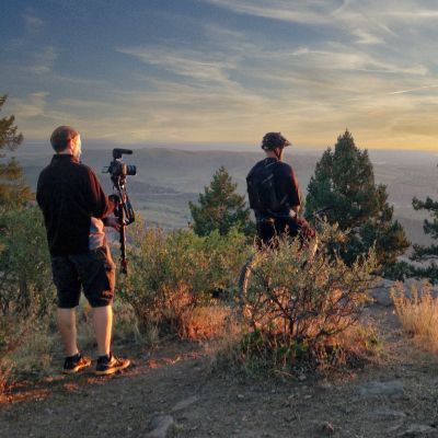 Two men standing on top of a hill with trees in the background