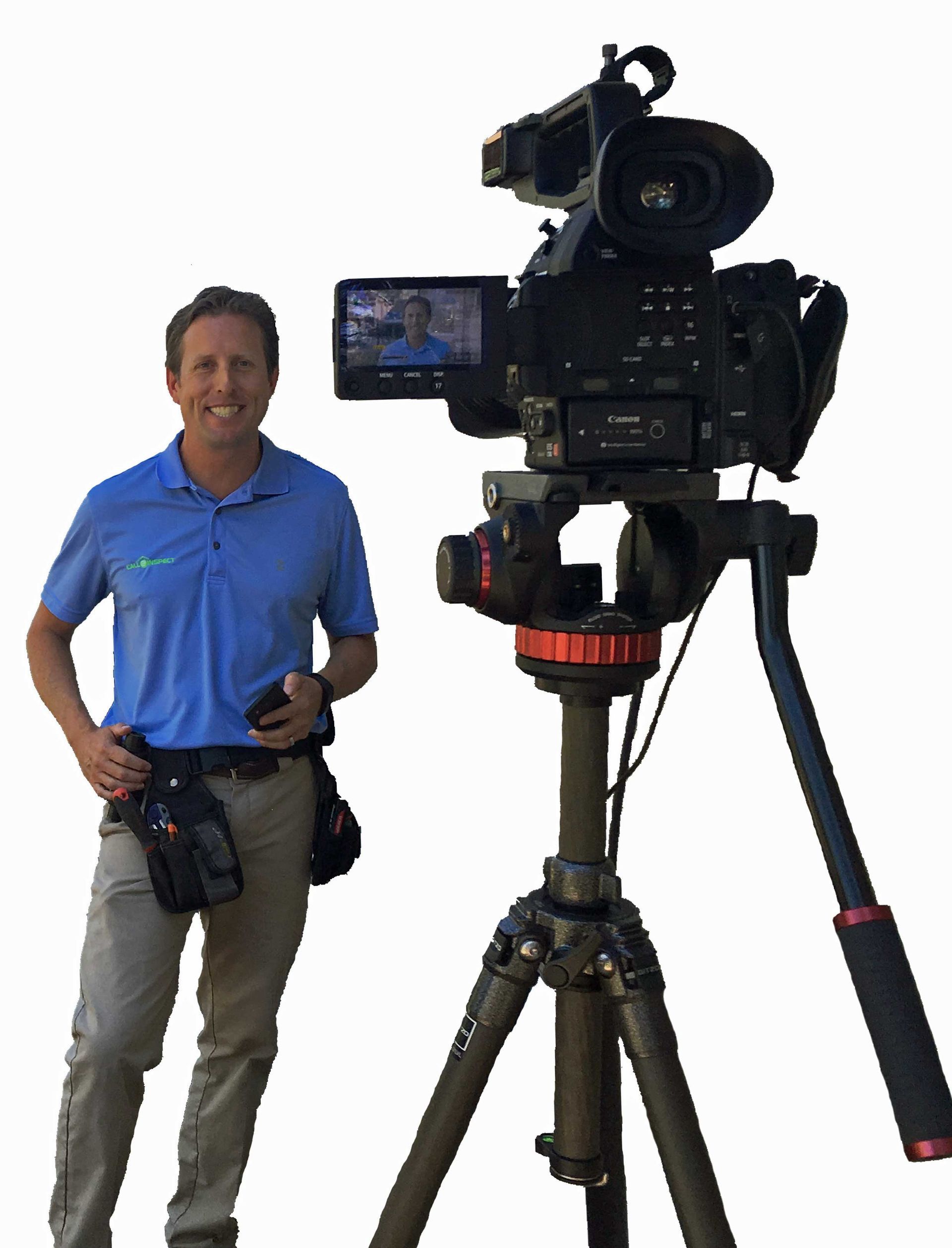 A man in a blue shirt is standing in front of a camera on a tripod.