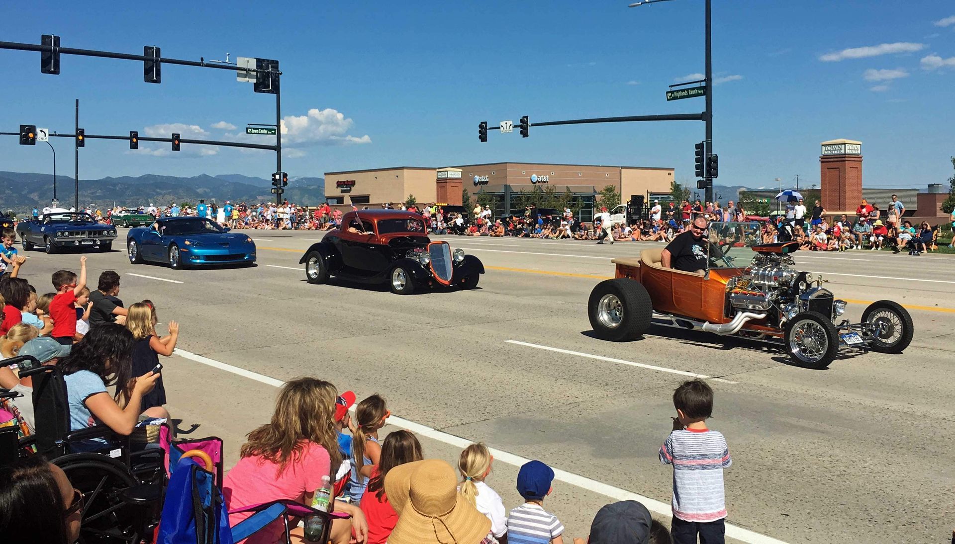 A parade with cars driving down the street with people watching.