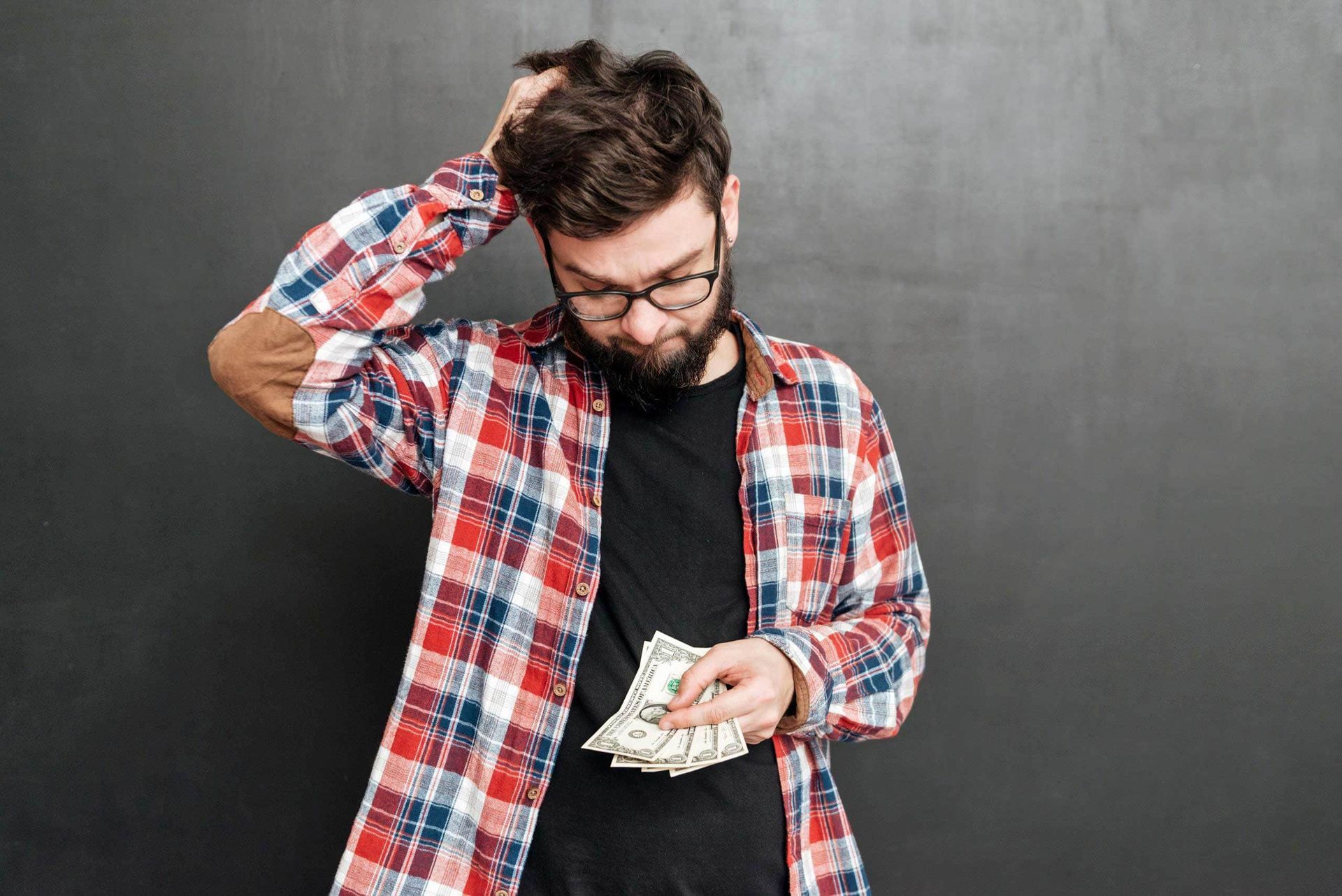 A man in a plaid shirt is holding a bunch of money in his hand.