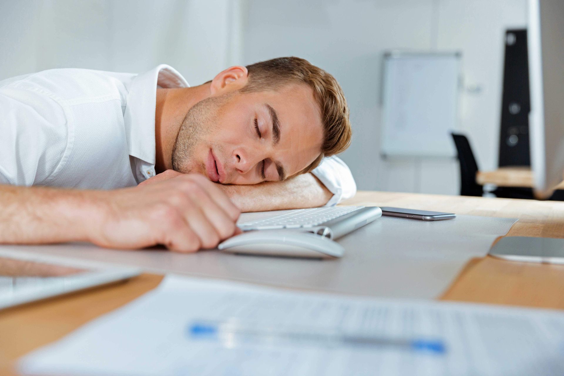 A man is sleeping at a desk with his head on a keyboard.