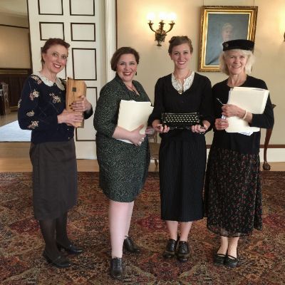 Four women standing next to each other holding papers and a keyboard