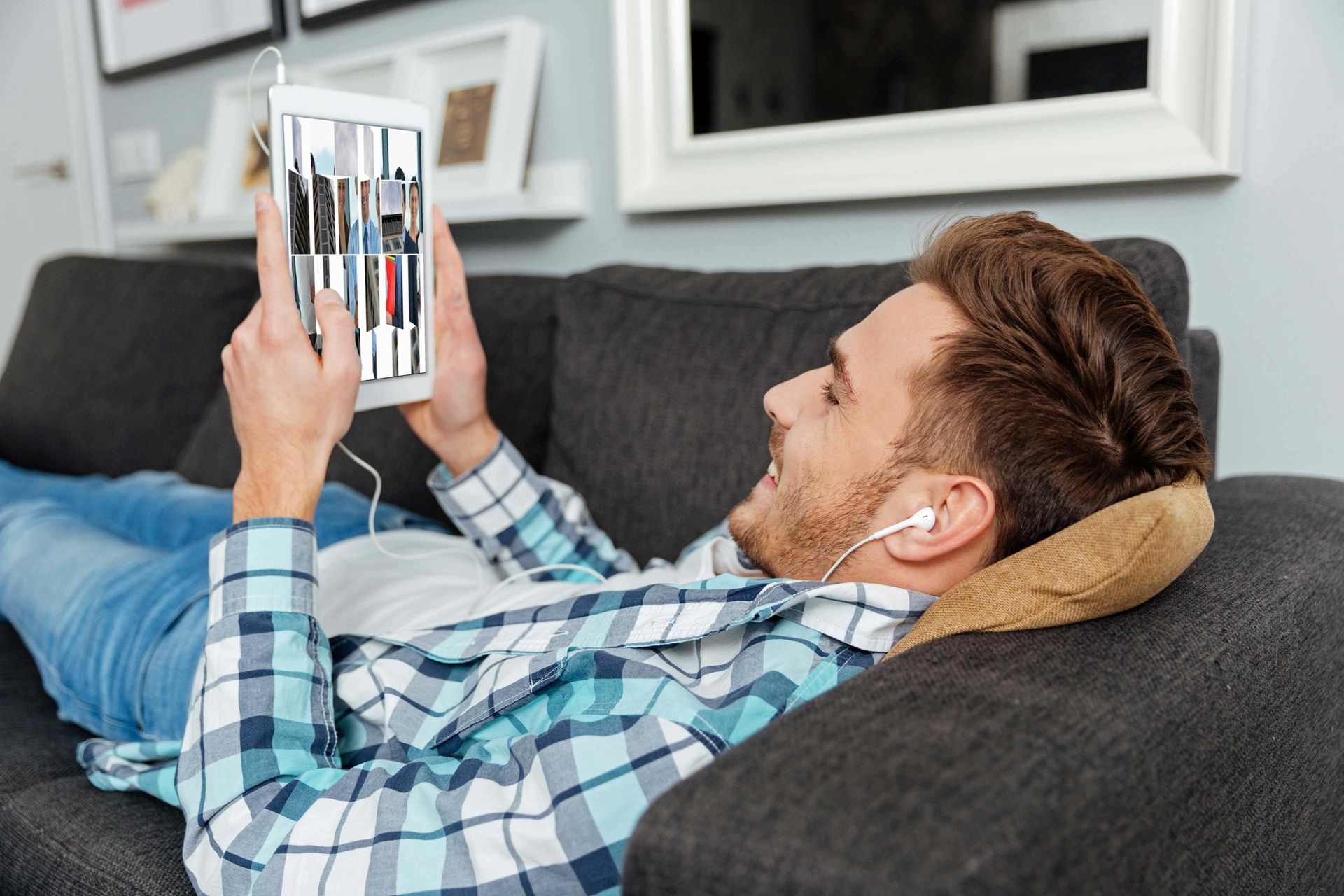 A man is laying on a couch using a tablet computer.