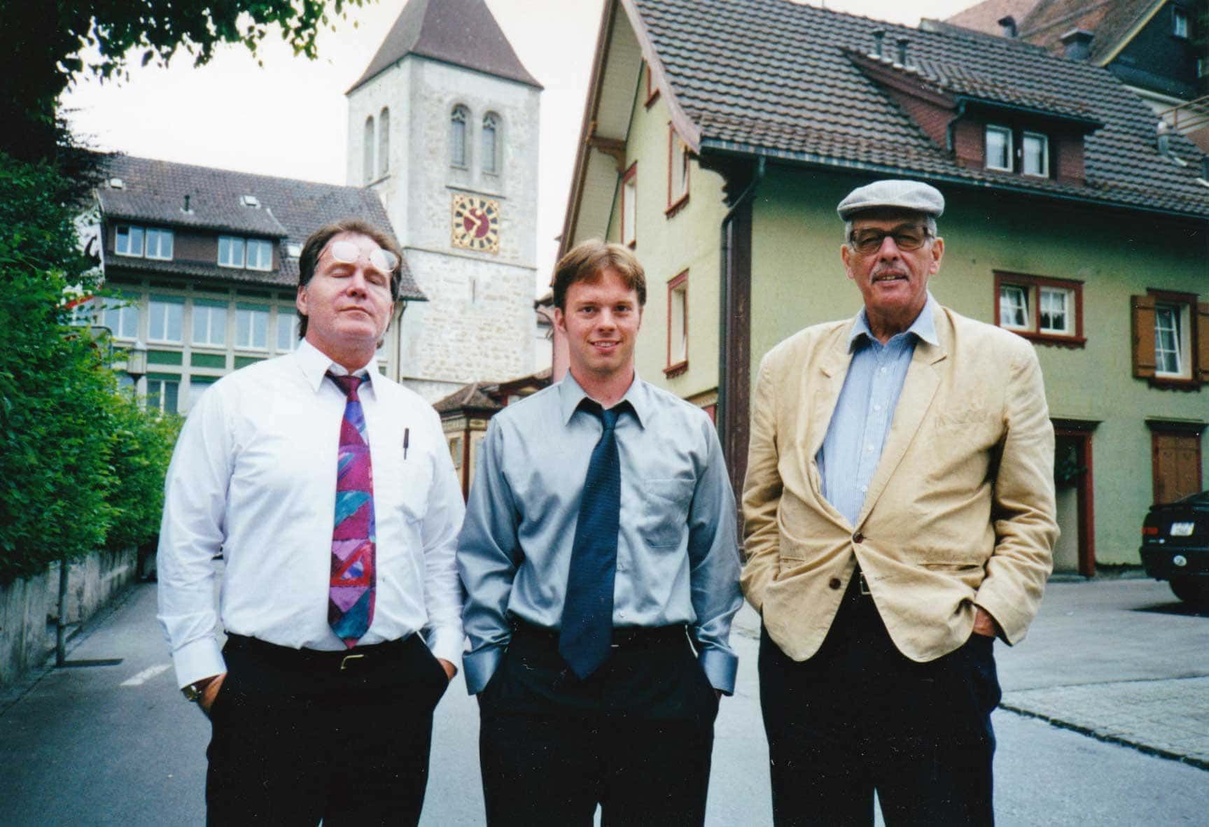 Three men standing in front of a building with a clock on it