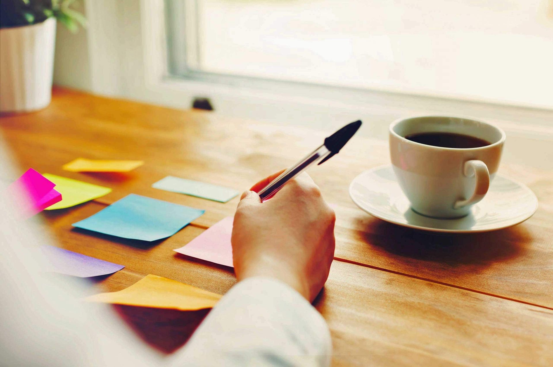 A person is writing on a piece of paper next to a cup of coffee.