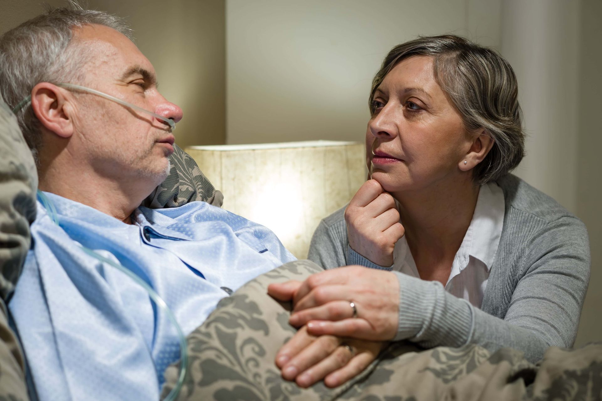 A woman is holding the hand of an elderly man in a hospital bed.