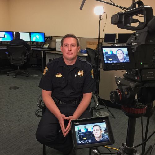 A man in a police uniform sits in front of a camera