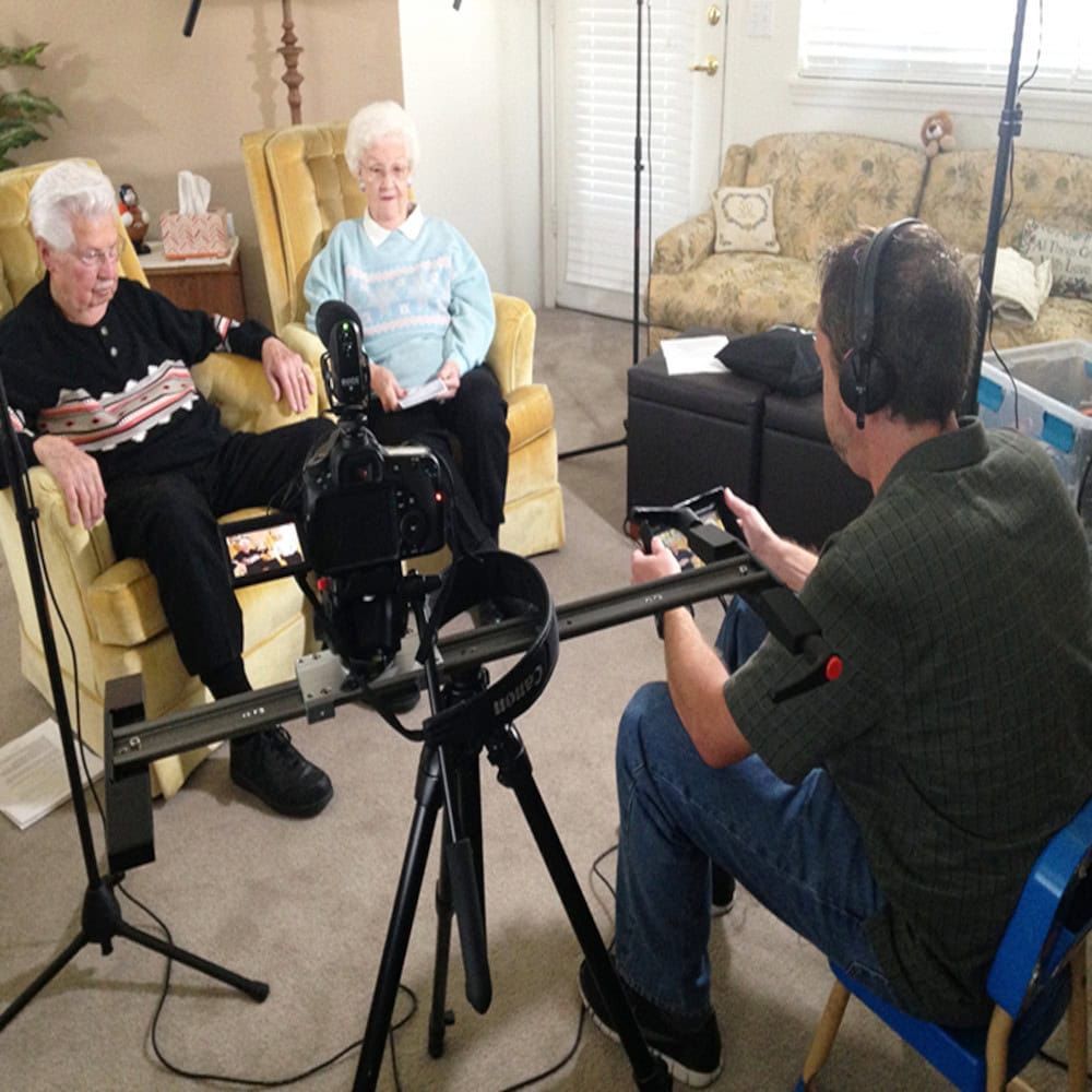 A man is sitting in front of a camera talking to two older women