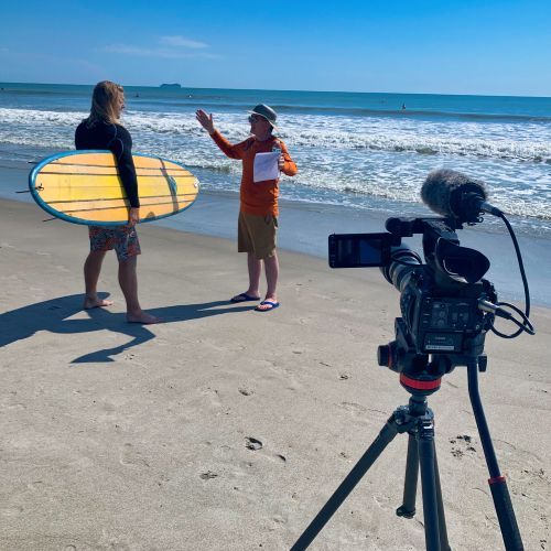 A man holding a surfboard talks to another man on the beach