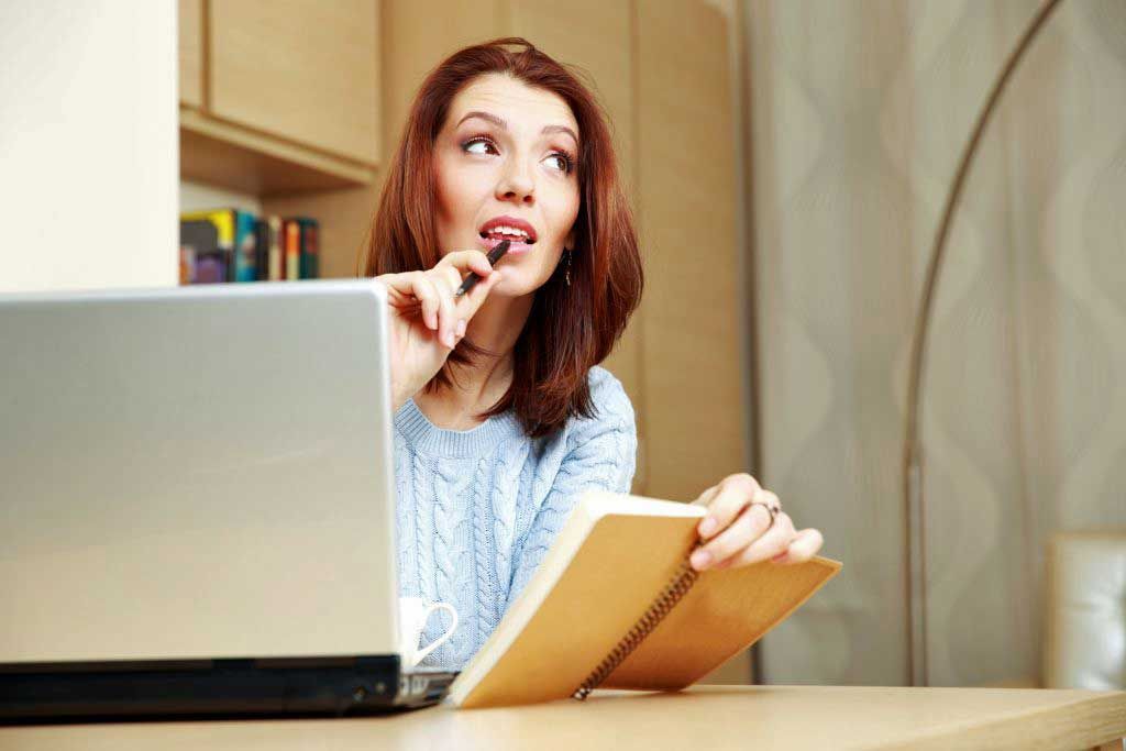 A woman is sitting at a desk with a notebook and a laptop.
