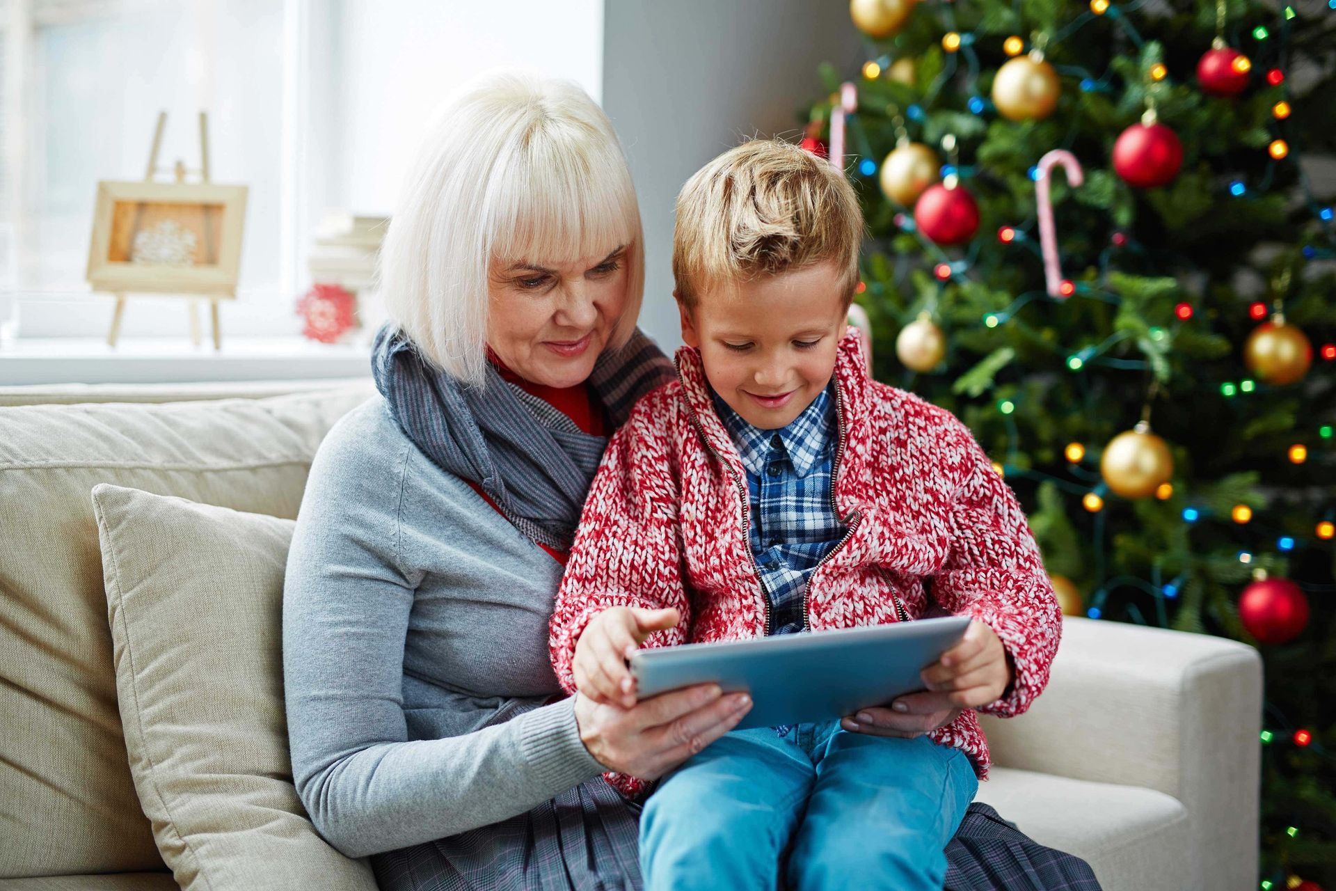 A woman and a child are sitting on a couch looking at a tablet.