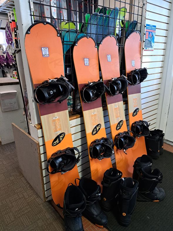 Orange snowboards with black bindings displayed in a retail shop, with black boots on the floor.