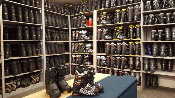 Wall of rows of black hockey skates in a store, with a few pairs displayed on a table in front.