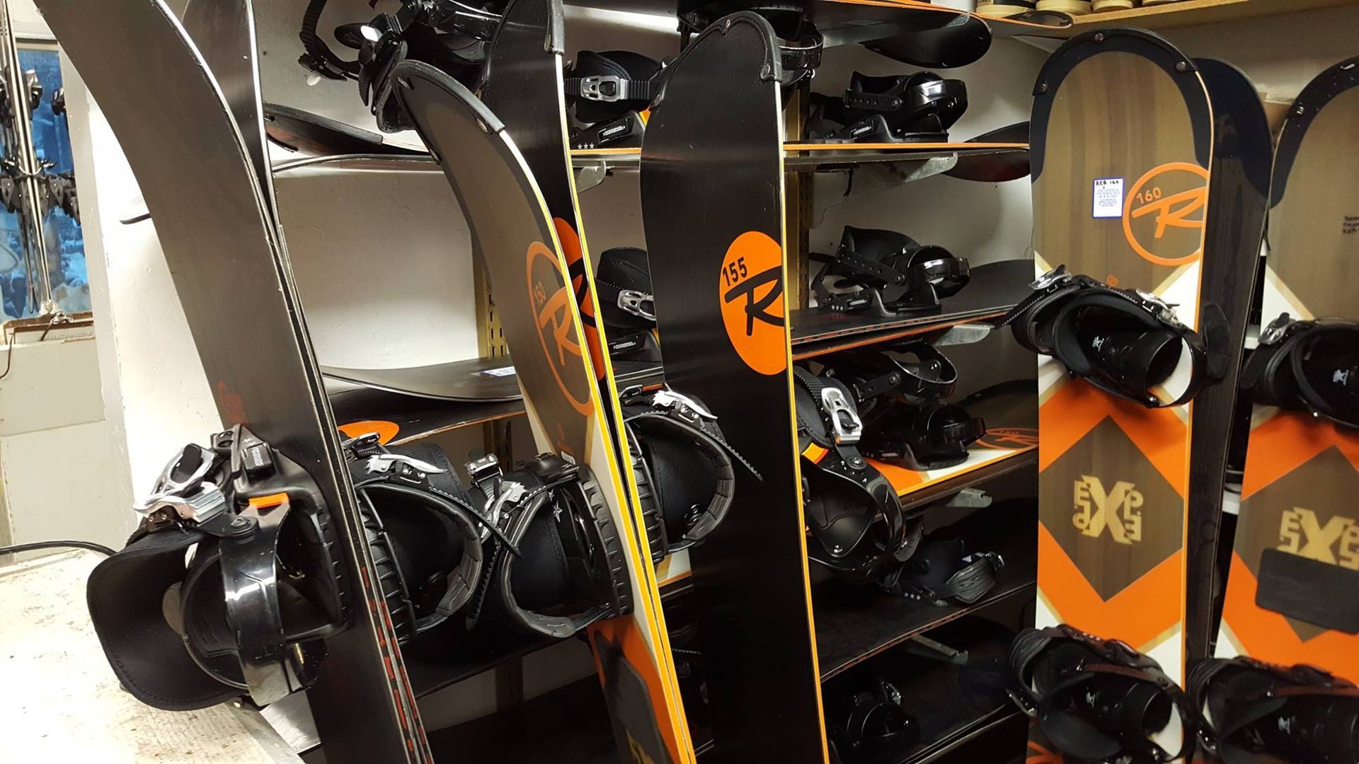 Ski and snowboard racks in a rental shop, with black and orange boards stacked vertically.