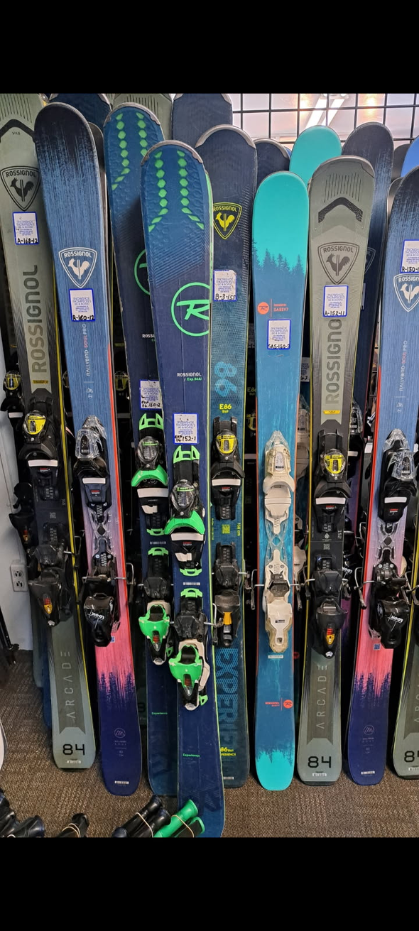 Row of colorful skis standing upright in a ski shop display, mostly black and neon yellow with some blue and pink pairs