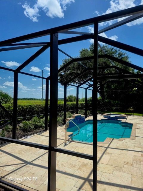 Screened patio overlooking a turquoise pool with stone deck and garden view under a blue sky