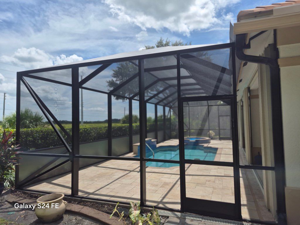 Worker installing a screened pool enclosure beside a backyard swimming pool