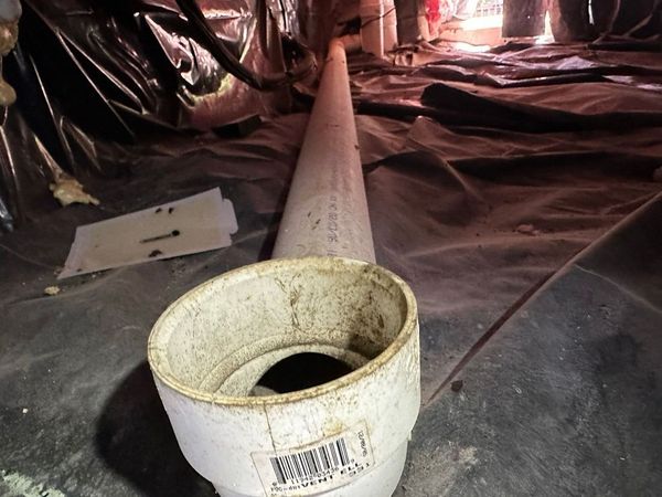 A long pipe runs through a crawlspace lined with black plastic sheeting.