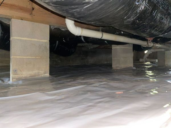 Crawlspace with concrete supports, white pipe, and black insulated ducting over a plastic-covered floor