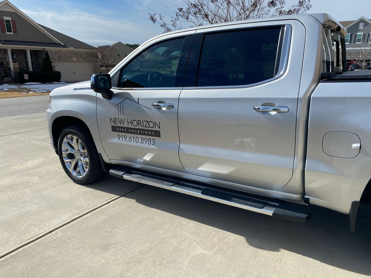 Silver pickup truck with company lettering parked in a driveway outside a house.