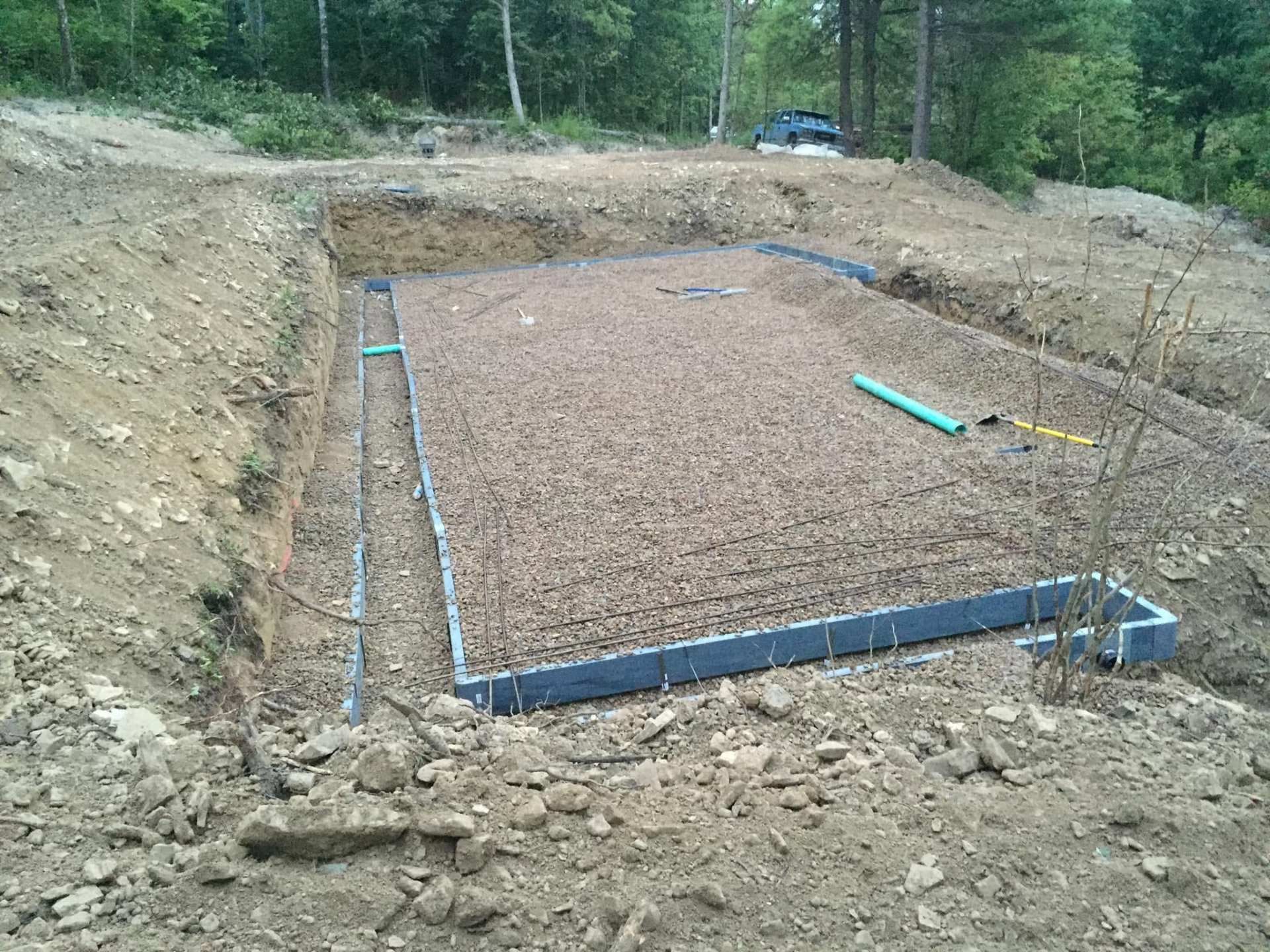 Gravel foundation pad bordered with blue edging at a wooded construction site